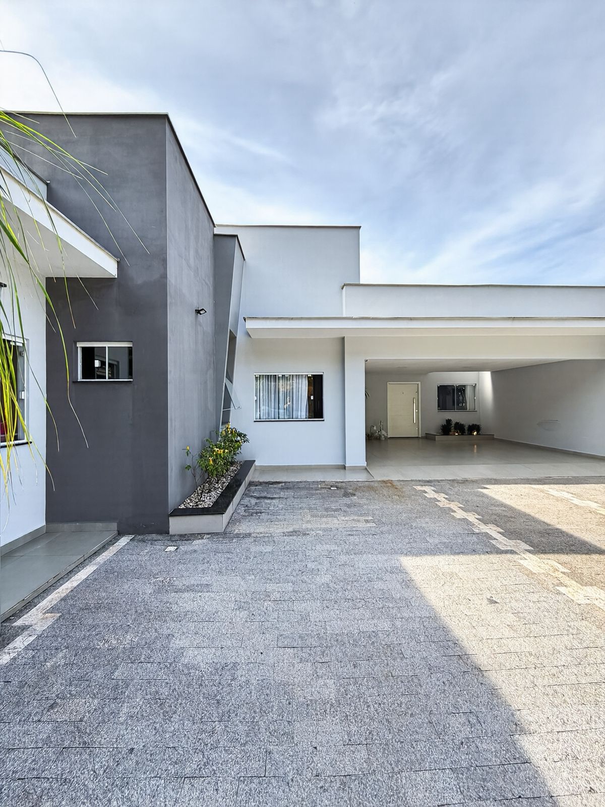 Vista lateral da casa com volume cinza, jardim e garagem ao fundo