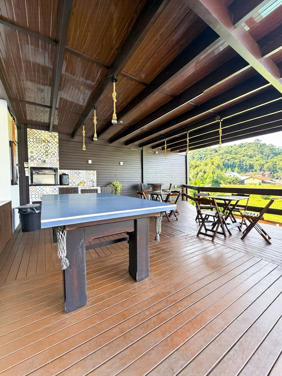 Área de festas coberta com mesa de ping pong, churrasqueira revestida de azulejos e vista para o vale