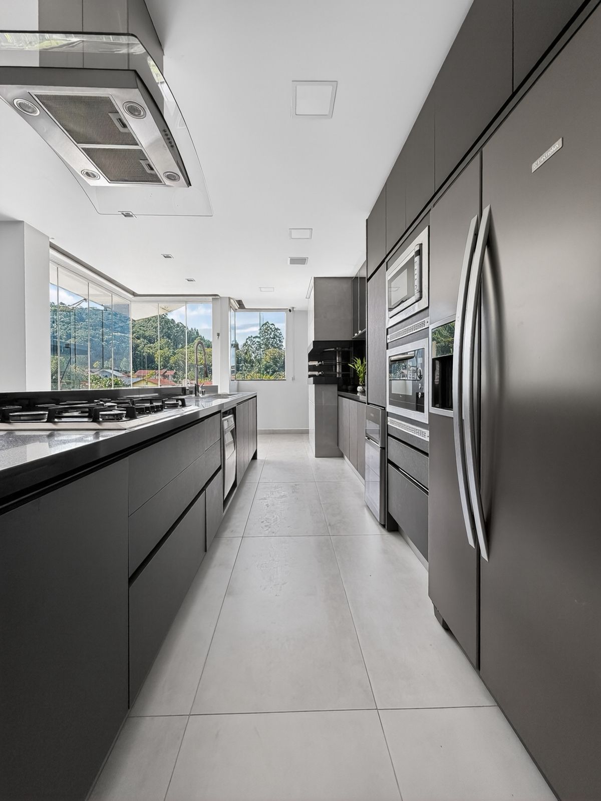 Cozinha com cooktop, coifa e janelas de vidro com vista para o vale