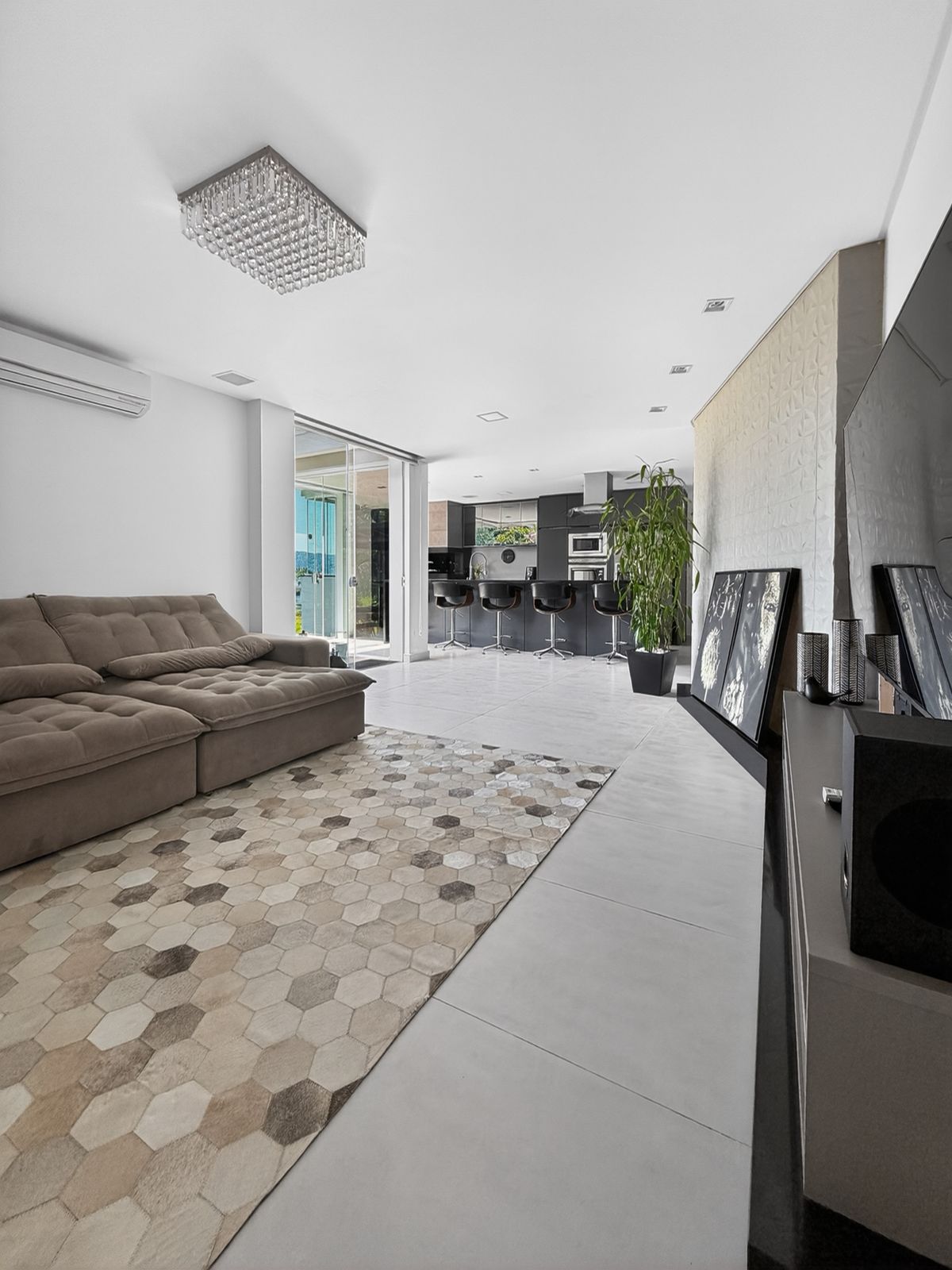 Sala de estar integrada à cozinha, com sofá, tapete e ar-condicionado