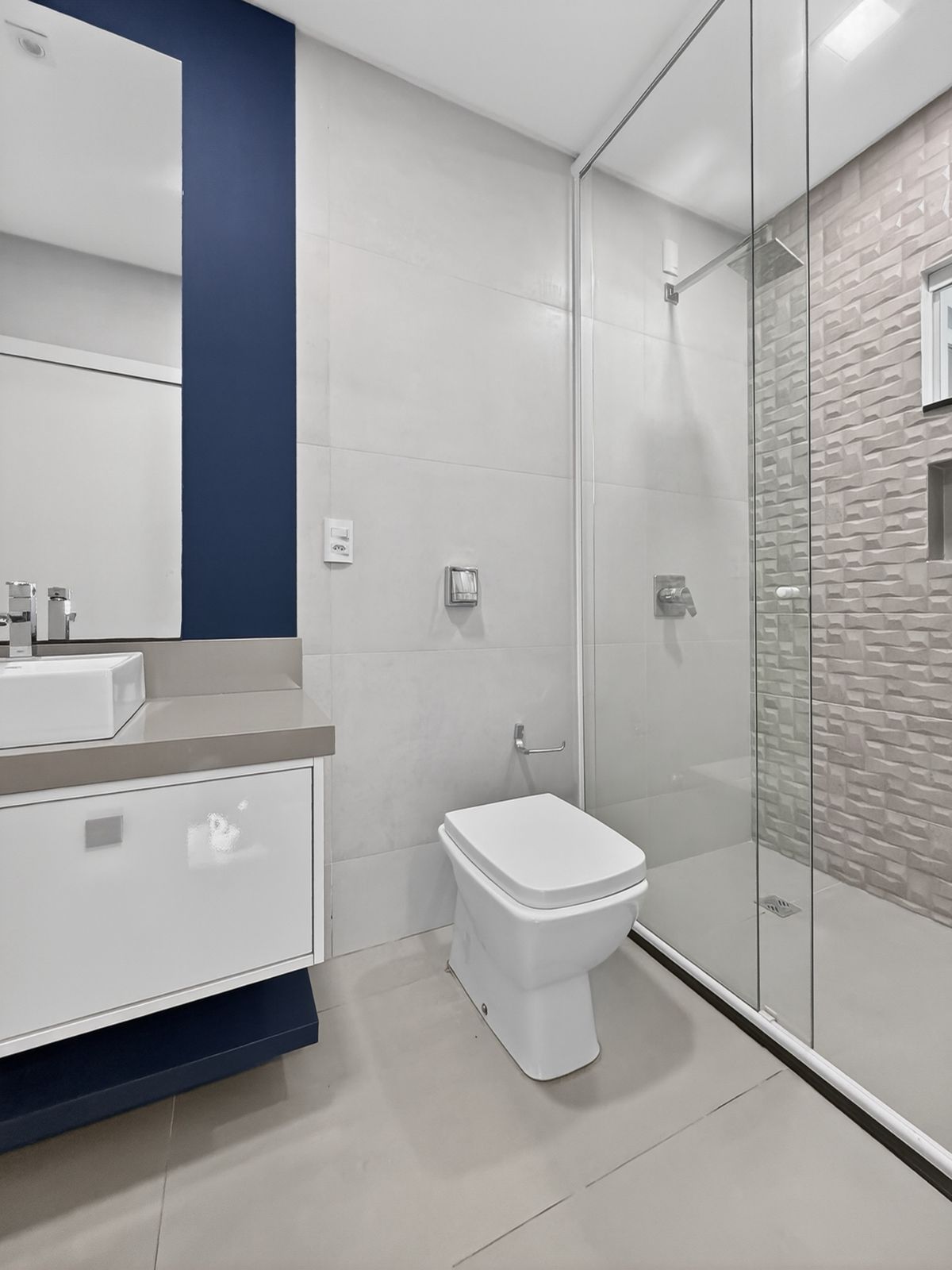 Banheiro da suíte com parede azul-marinho, box de vidro e revestimento 3D