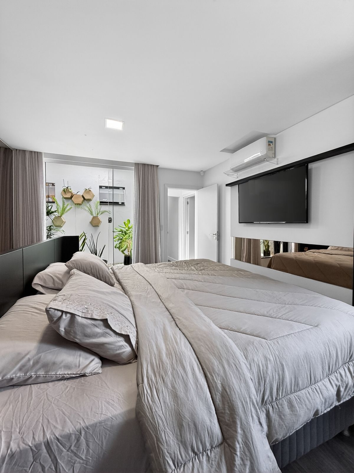 Suíte master com cama de casal, TV, ar-condicionado e jardim de inverno ao fundo