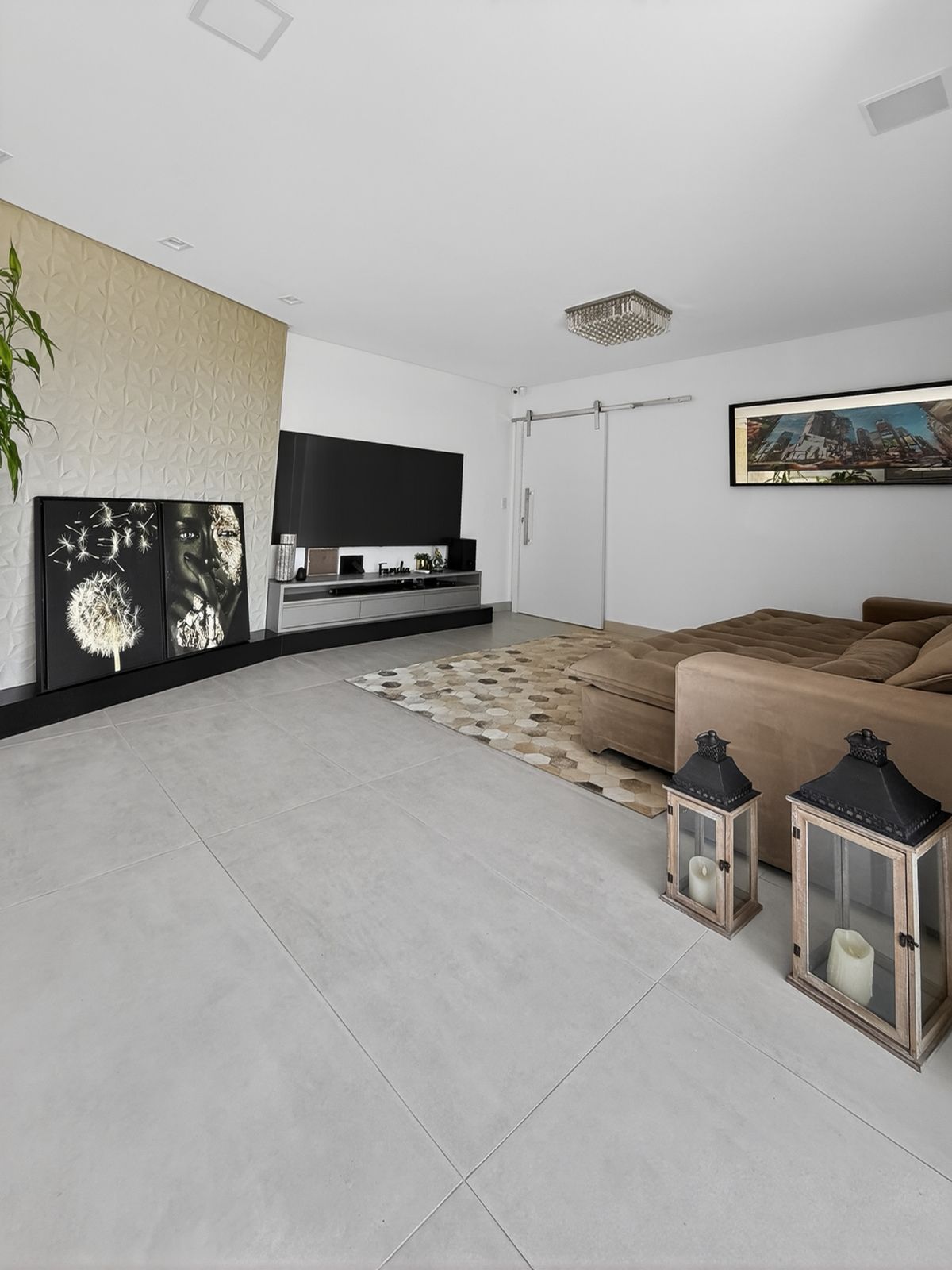 Sala de estar com TV grande no painel 3D, rack, sofá e porta de correr