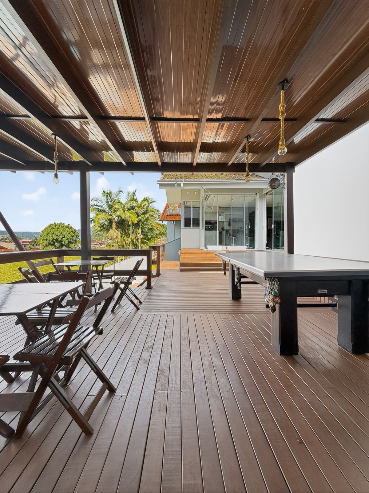 Área de festas coberta com mesas, deck de madeira e vista para a casa e o vale