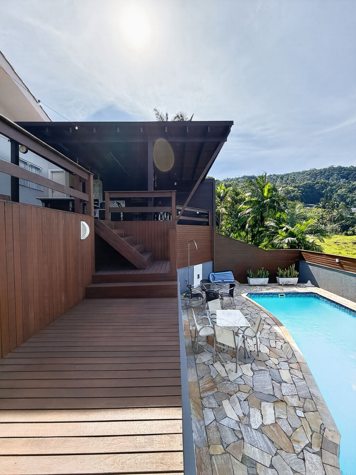 Deck de madeira com escada de acesso e piscina ao lado, com o morro ao fundo