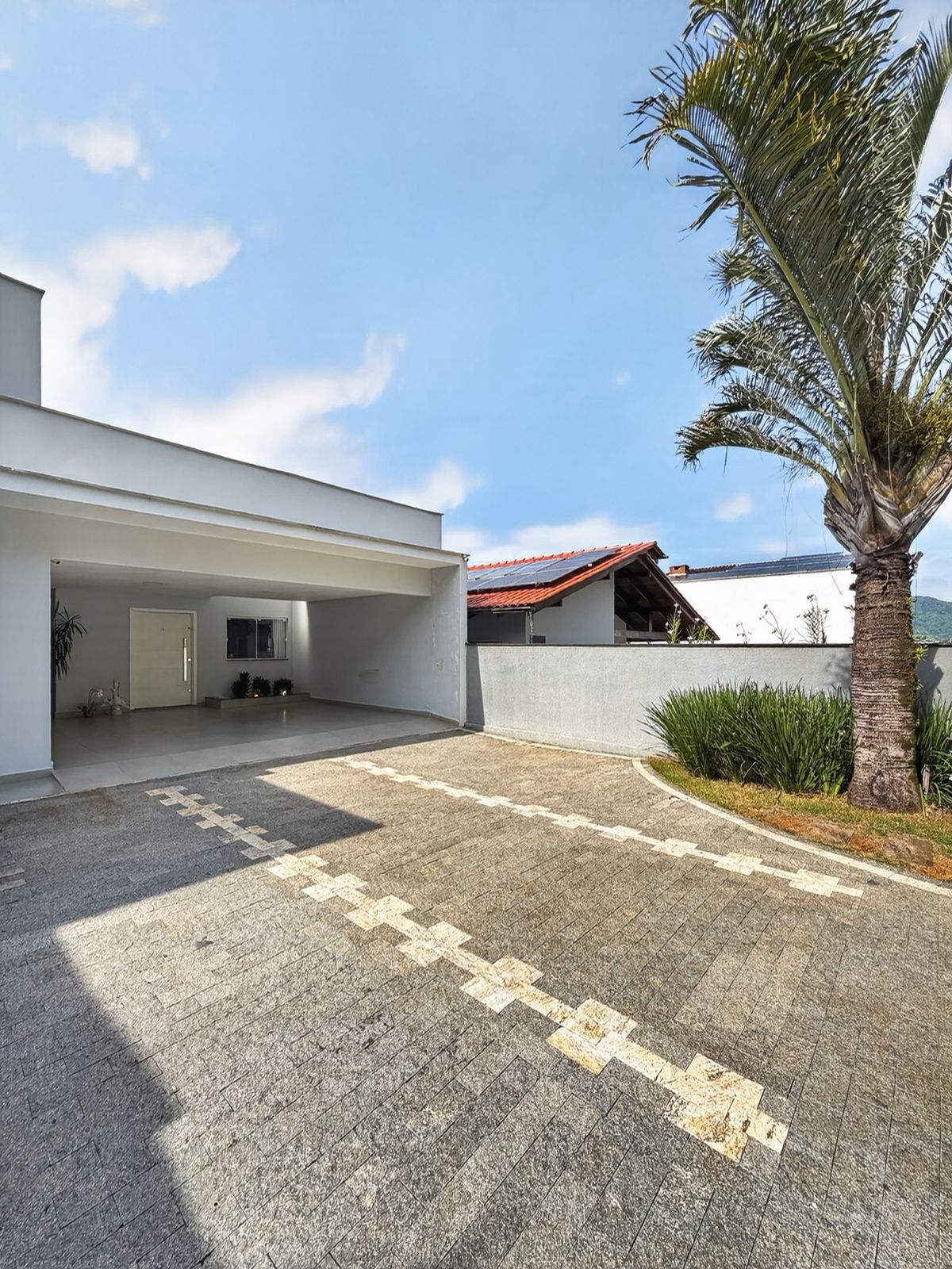 Garagem coberta ampla com palmeira e jardim na entrada da casa