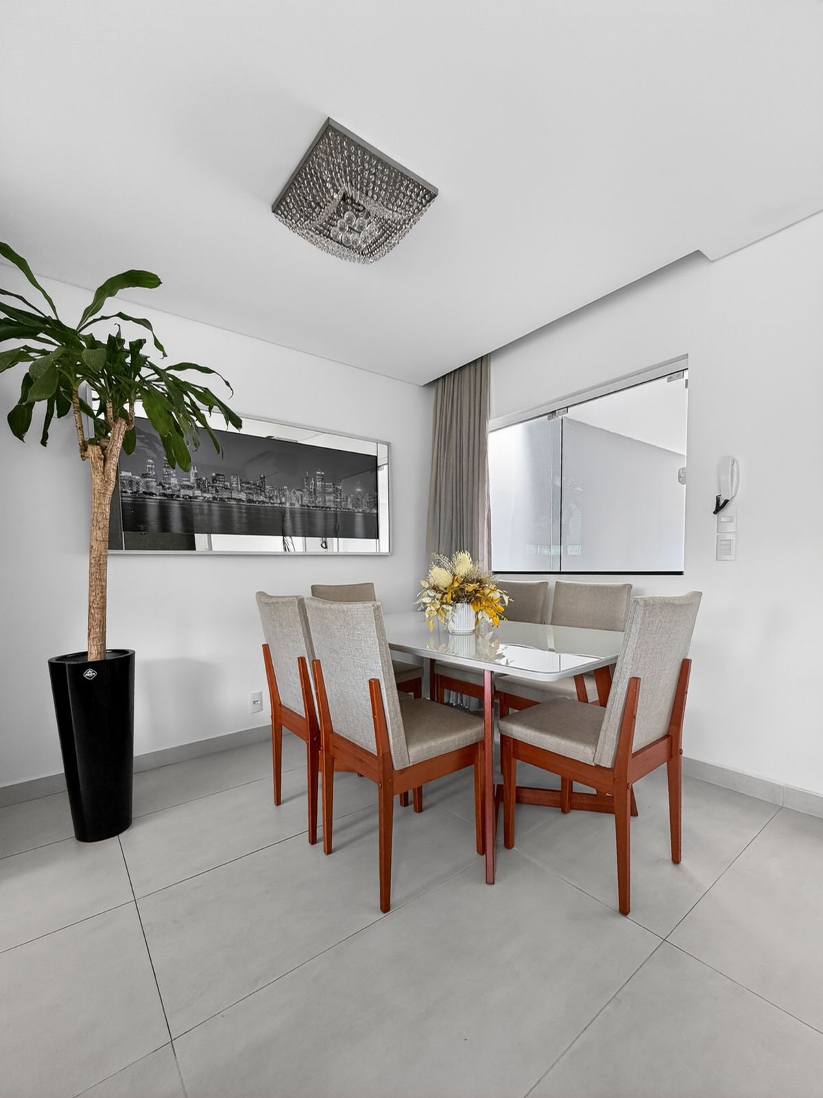 Sala de jantar com mesa branca para seis lugares, lustre de cristal e janelas amplas